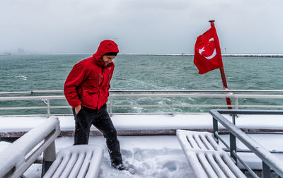 Woman standing by railing against sea during winter