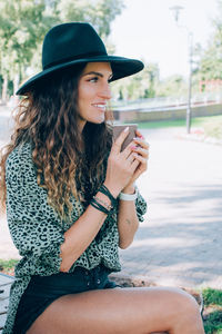 Portrait of beautiful stylish young woman wearing black felt hat drinking coffee. .