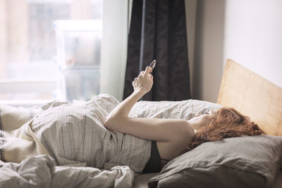 Woman using smart phone while lying on bed