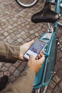 Cropped hands of senior man scanning qr code of bicycle while through smart phone at parking station