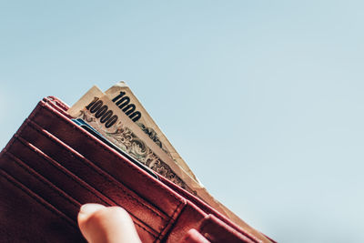 Low angle view of hand holding book against clear sky