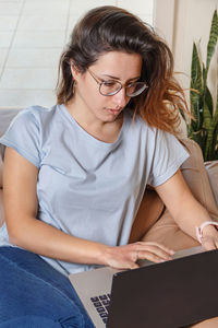 Young woman using laptop while sitting on sofa at home