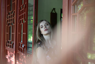 Portrait of young woman looking through window