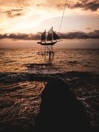 Silhouette sailboat on beach against sky during sunset