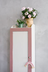 A pencil case cabinet in the children's room with flowers in a vase on it and a watering can