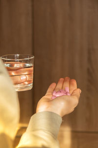 Female hand holding glass of water and pink pill. collagen supplement for nutrition. healthy eating