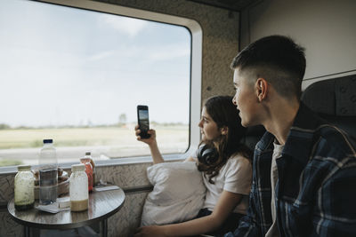 Boy looking at sister photographing through smart phone in train