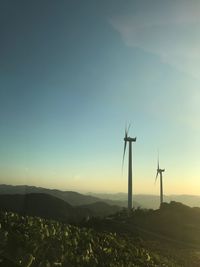 Wind turbines on land against sky during sunset