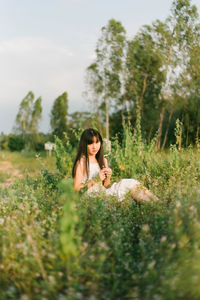 Portrait of woman sitting on grassy land against sky