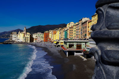 Buildings by sea against clear blue sky