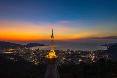 Illuminated tower amidst buildings against sky during sunset