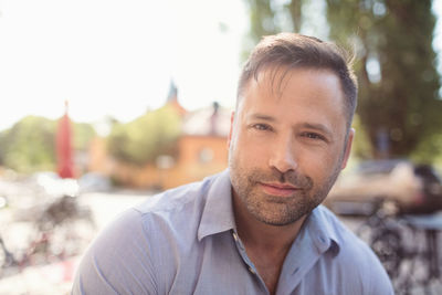 Portrait of confident businessman listening music through in-ear headphones on sunny day