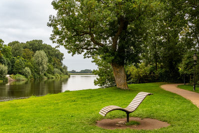 Park bench by lake against sky