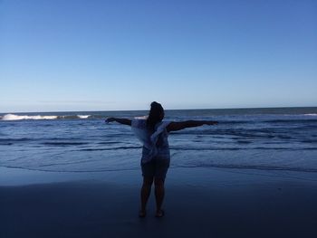 Rear view of woman standing on beach against clear sky