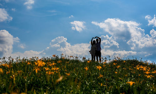 Silhouette couple standing on land against sky during sunny day