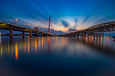 Illuminated bridge over river against sky during sunset