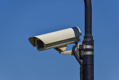 Low angle view of security camera against clear blue sky