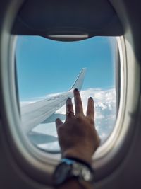 Cropped image of hand against sky seen through airplane window