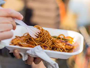 Cropped hand holding fork and noodles plate