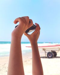 Cropped hands holding mobile phone at beach