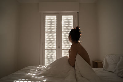 Rear view of woman sitting on bed