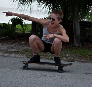 Full length of happy woman pointing on longboard