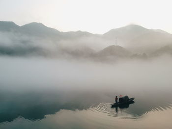 Silhouette man on boat in lake against mountains during foggy weather