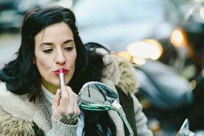 Woman applying lipstick while looking in vehicle mirror