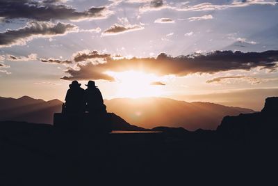 Silhouette man and a woman standing on mountain against sky during sunset