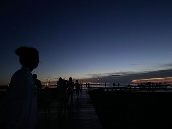 Silhouette people standing by railing against sky during sunset