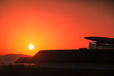 Silhouette built structure against orange sky