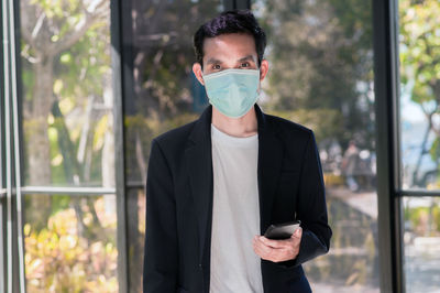 Portrait of young man standing against window