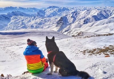 Rear view of man with dog sitting on snow covered field