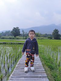 Boy standing on boardwalk against sky