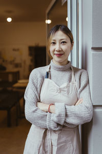 Portrait of female potter standing with arms crossed at workshop doorway