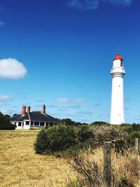 Lighthouse on field by building against sky