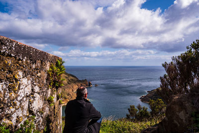 Rear view of man siting against sea and sky