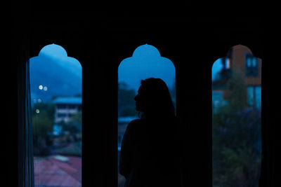 Rear view of silhouette man standing against window