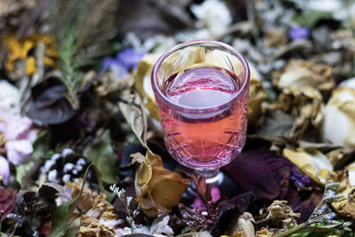 A small wine glass filled with red liquid. placed on assorted dried flowers and blurred alternately