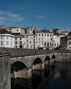 Arch bridge over river by buildings against sky in city