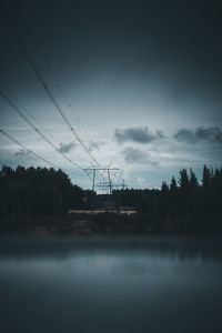 Electricity pylon by trees against sky