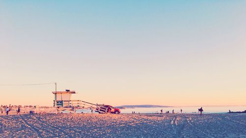 People on beach against clear sky during sunset