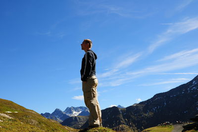 Full length of hiker standing on field by mountain against sky