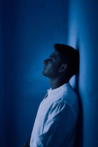 Side view of young man looking away against blue wall