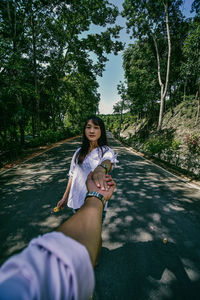 Portrait of woman smiling while holding plant against trees