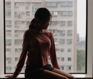 Young woman sitting on window sill