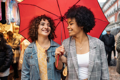 Happy young woman holding umbrella in city