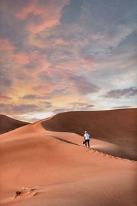 Man on sand dune in desert against sky