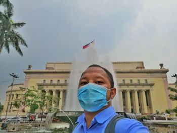 Portrait of man standing by building against sky