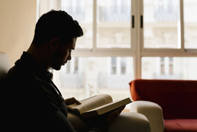 Young man sitting on sofa reading book at home